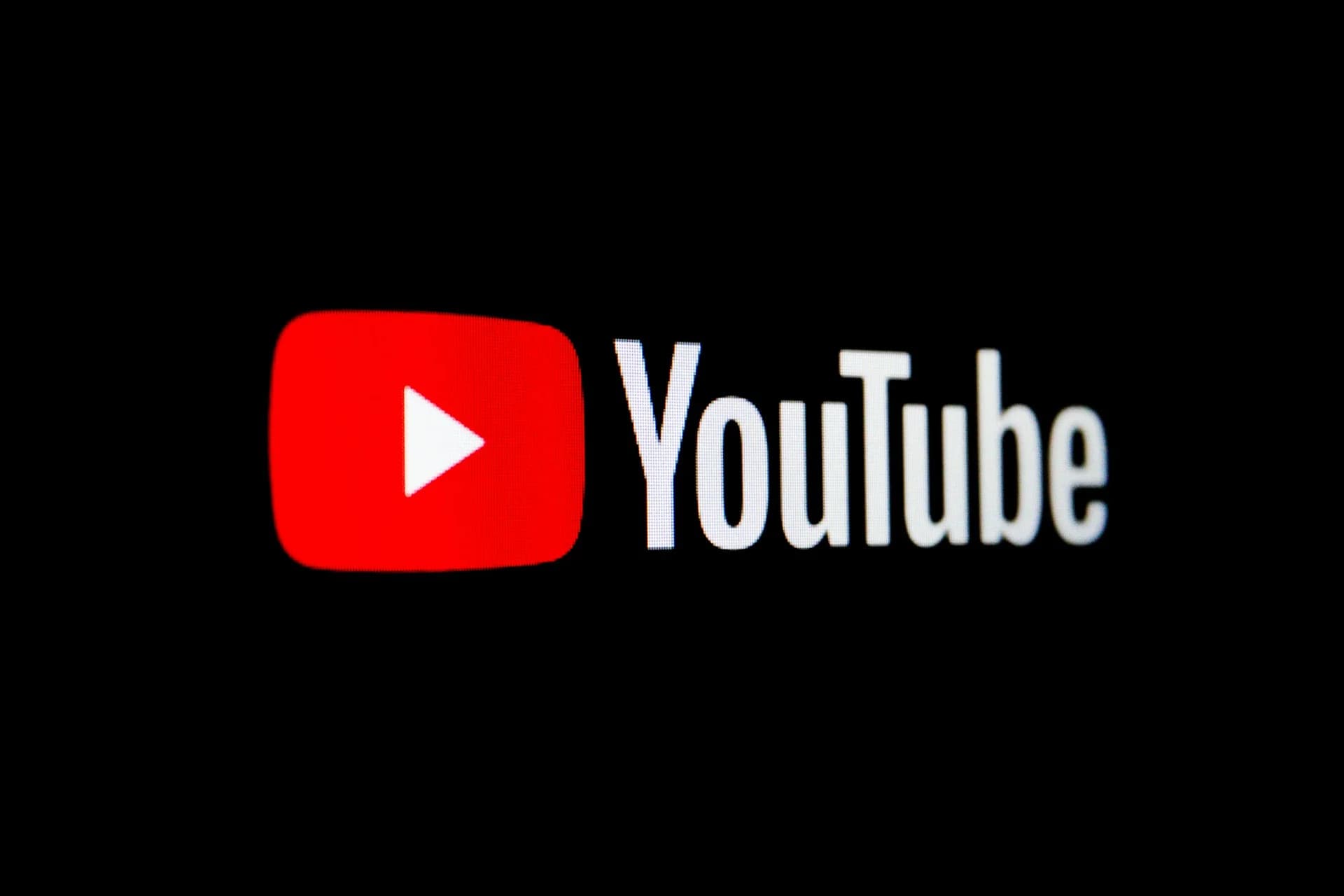 YouTubes röda uppspelningssymbol och vita ordmärke fotograferade på en svart skärm.