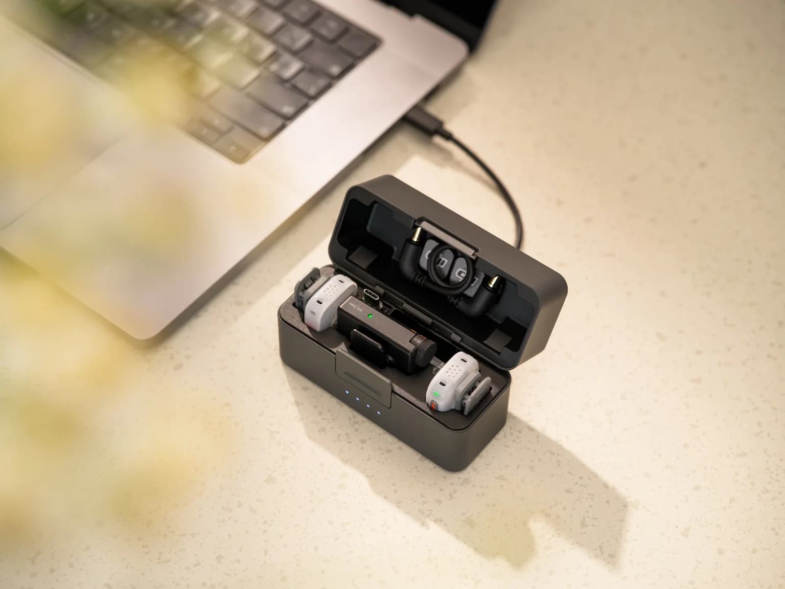 DJI Mic Mini 2S med två sändare och mottagare i det öppna laddningsetuiet bredvid en bärbar dator.