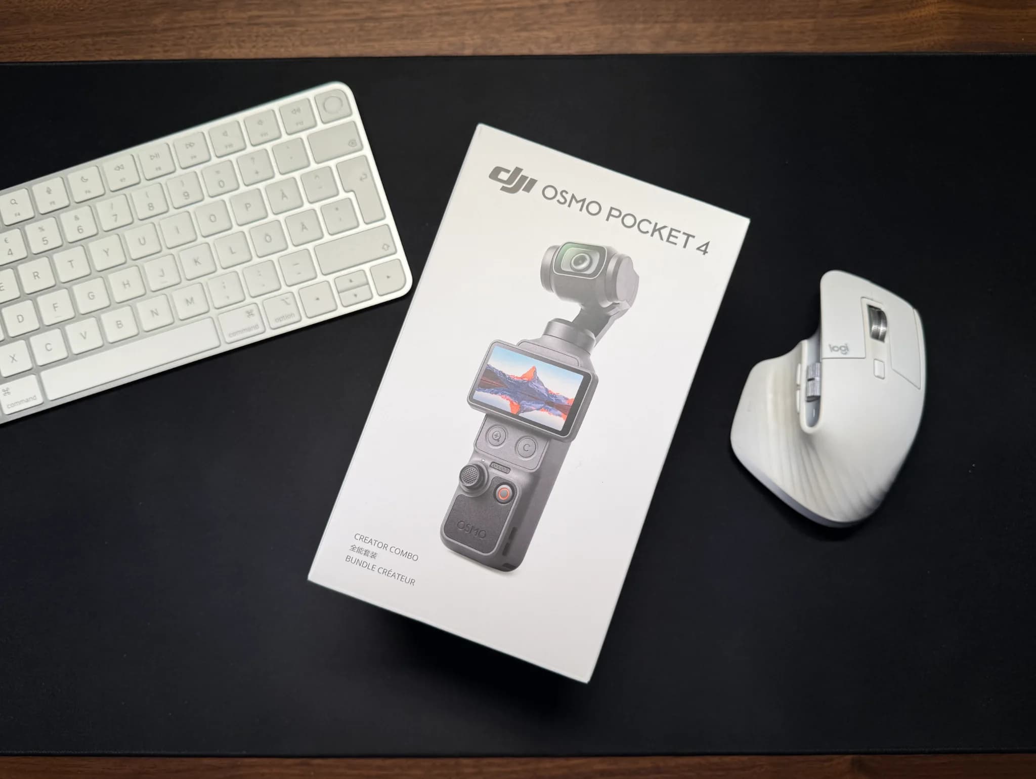 Förpackningen till DJI Osmo Pocket 4 Creator Combo ligger på en svart skrivbordsmatta bredvid ett tangentbord och en mus.