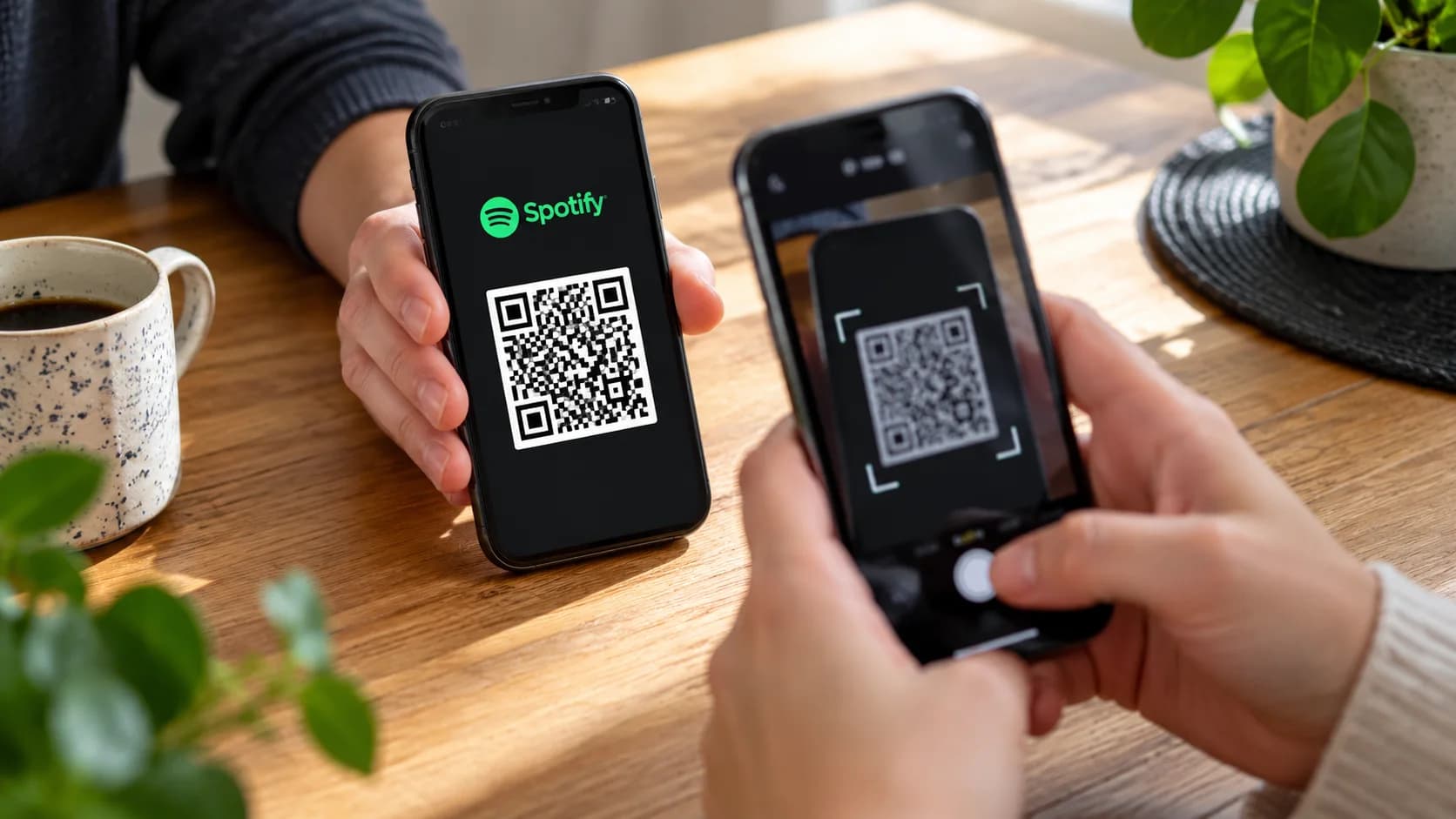 Två personer håller varsin mobiltelefon och skannar en illustrativ QR-kod vid ett träbord.