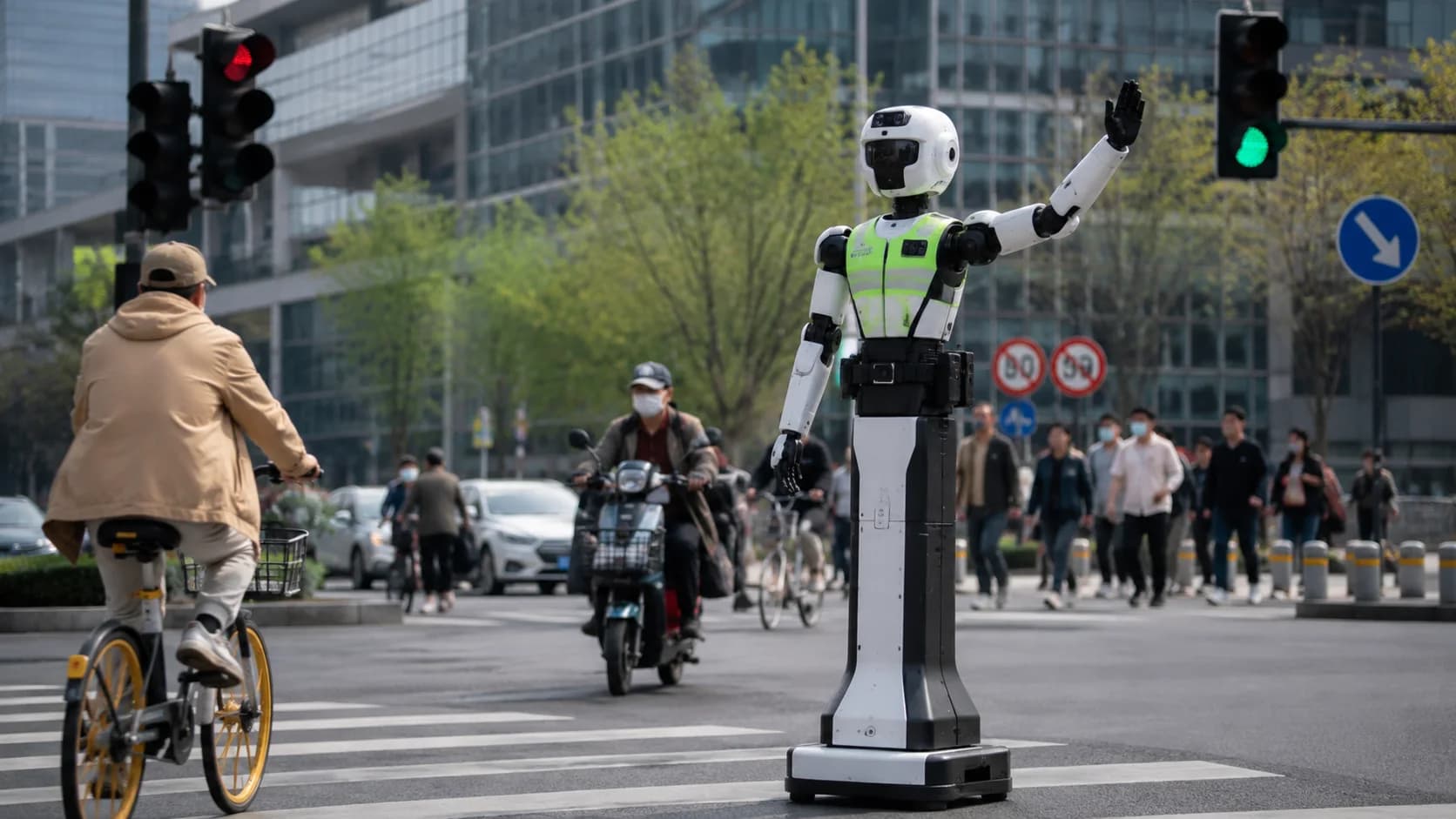 En hög humanoid robot i reflexväst dirigerar cyklister och fotgängare vid en trafikerad stadskorsning i Kina.