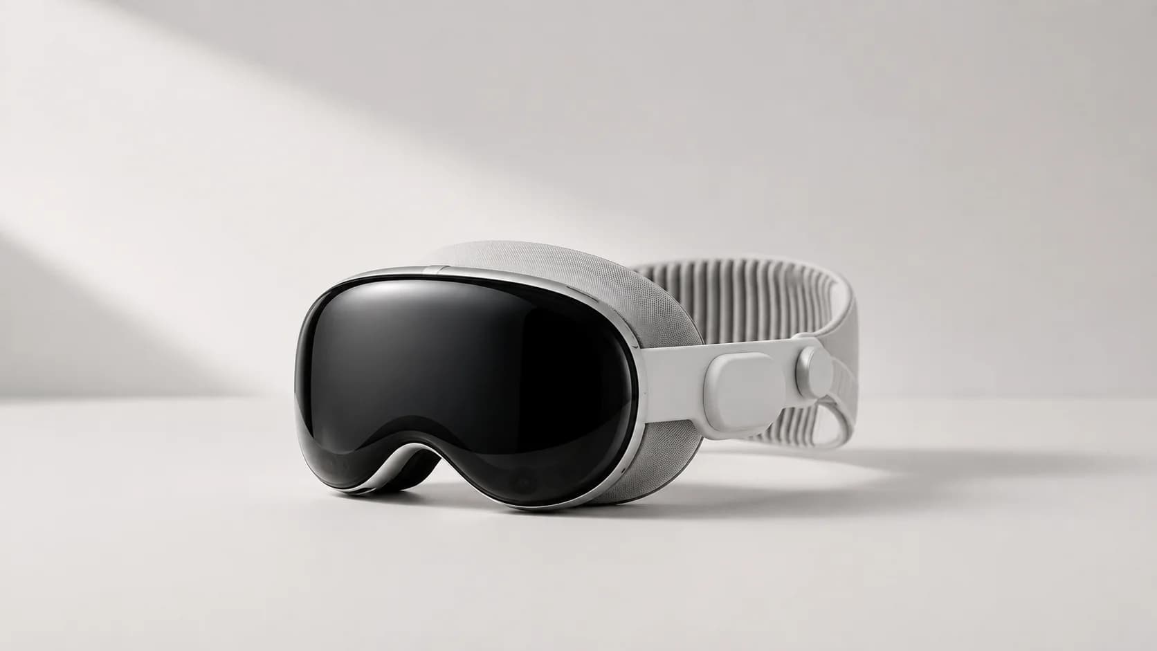 Ett ljust headset för rumslig datoranvändning med svart välvd front och gråvit rem ligger på en ljus neutral yta.
