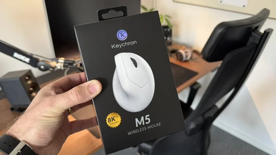 Kartongen till den vita Keychron M5 8K hålls upp centrerad framför ett skrivbord.