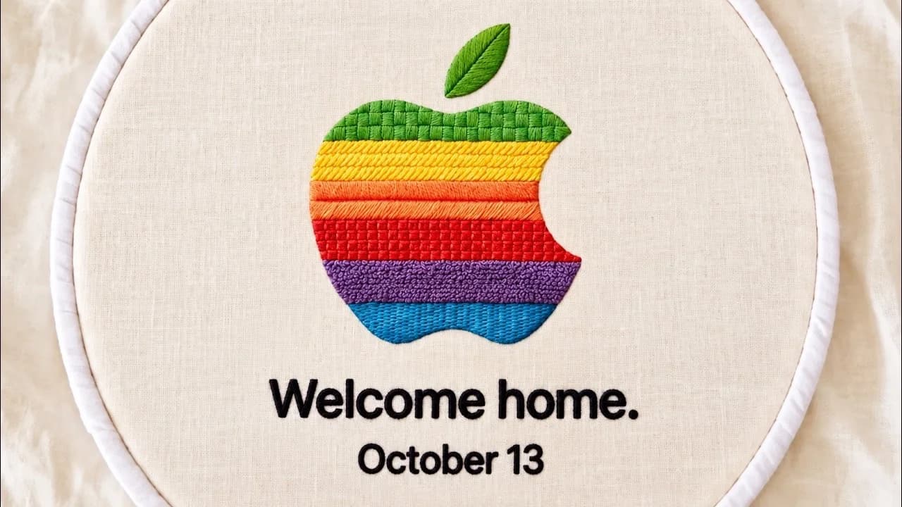 Broderad regnbågsfärgad Apple-logotyp med texten Welcome home. October 13 på ljust tyg i en broderiram.
