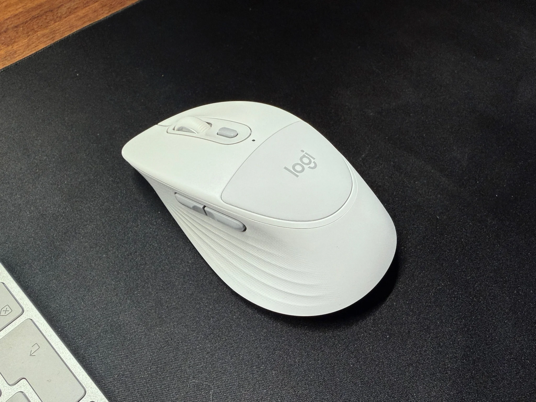 Logitech Signature Comfort Plus M850 L ligger på en svart skrivbordsmatta bredvid ett tangentbord.