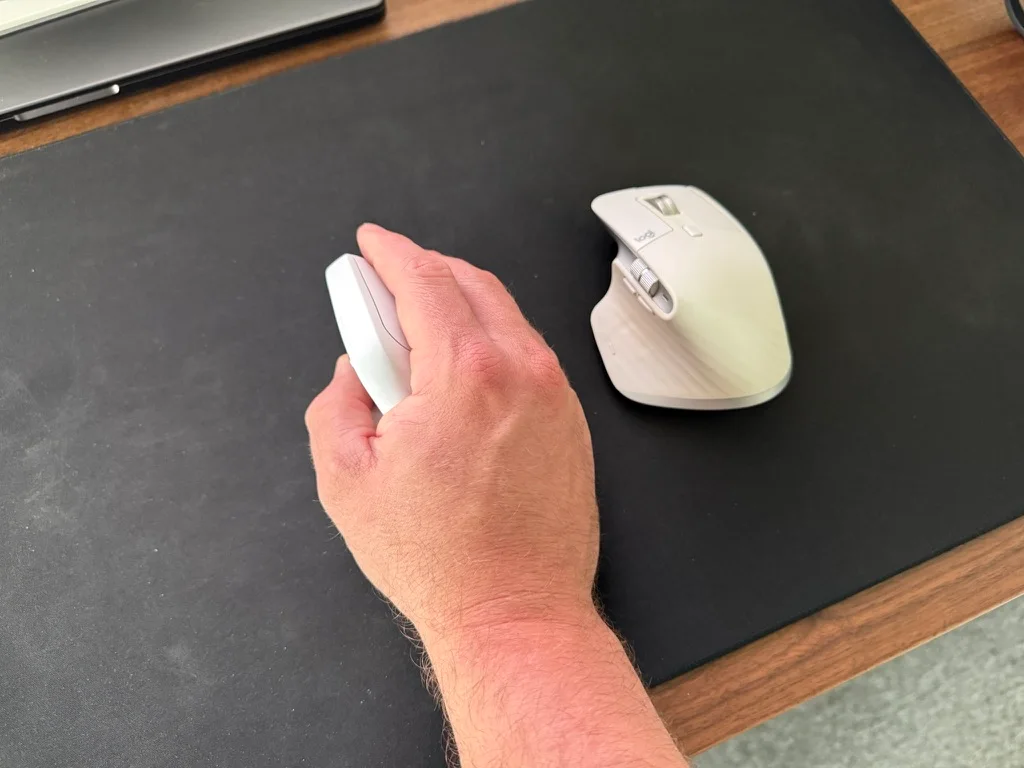 Keychron M5 8K används med höger hand på en musmatta bredvid en traditionell mus.