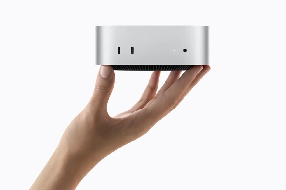 En hand håller nya Mac mini i silver med de två USB-C-portarna och hörlursuttaget synliga på framsidan.