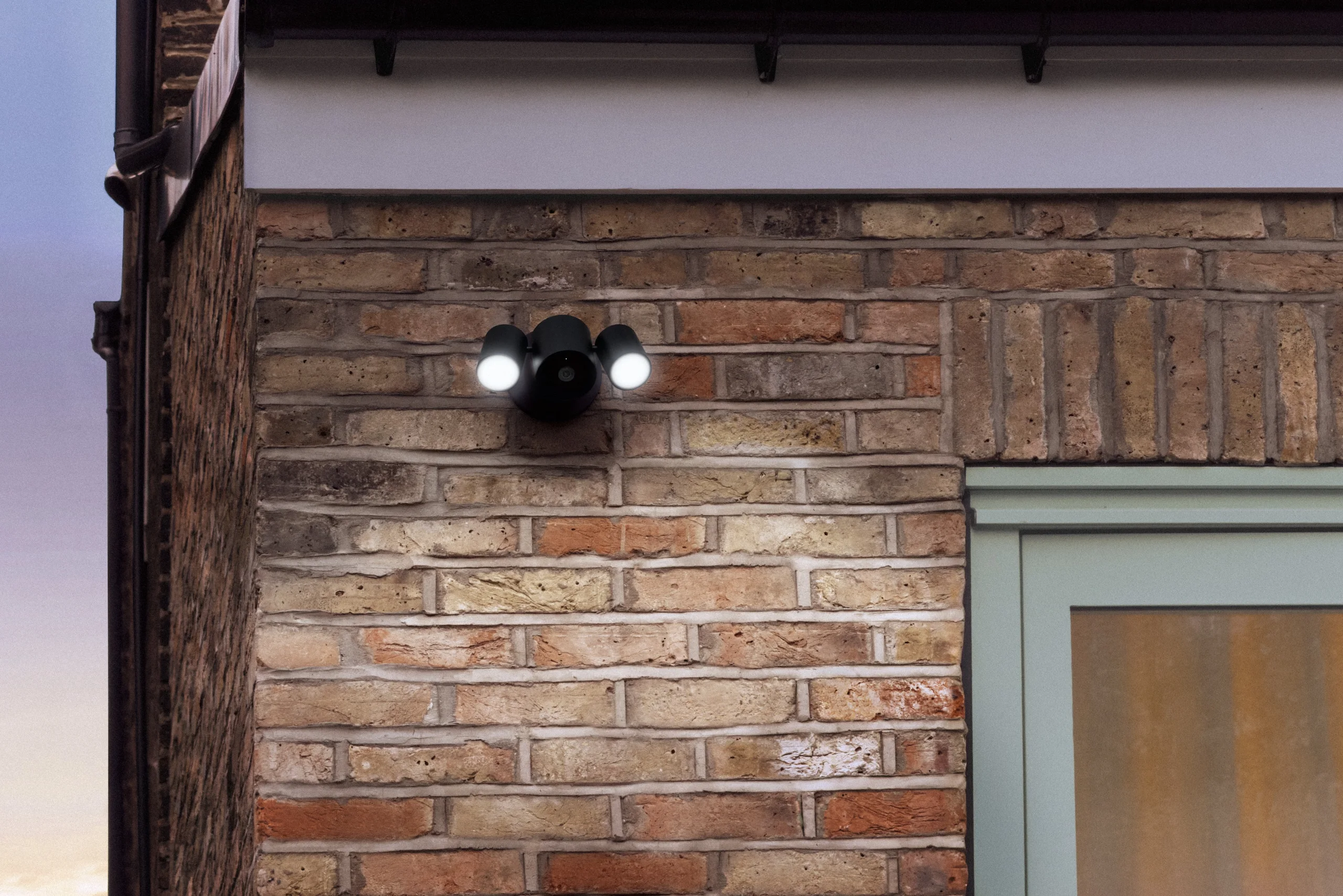 LG:s Floodlight Cam med två tända strålkastare monterad på en tegelfasad.