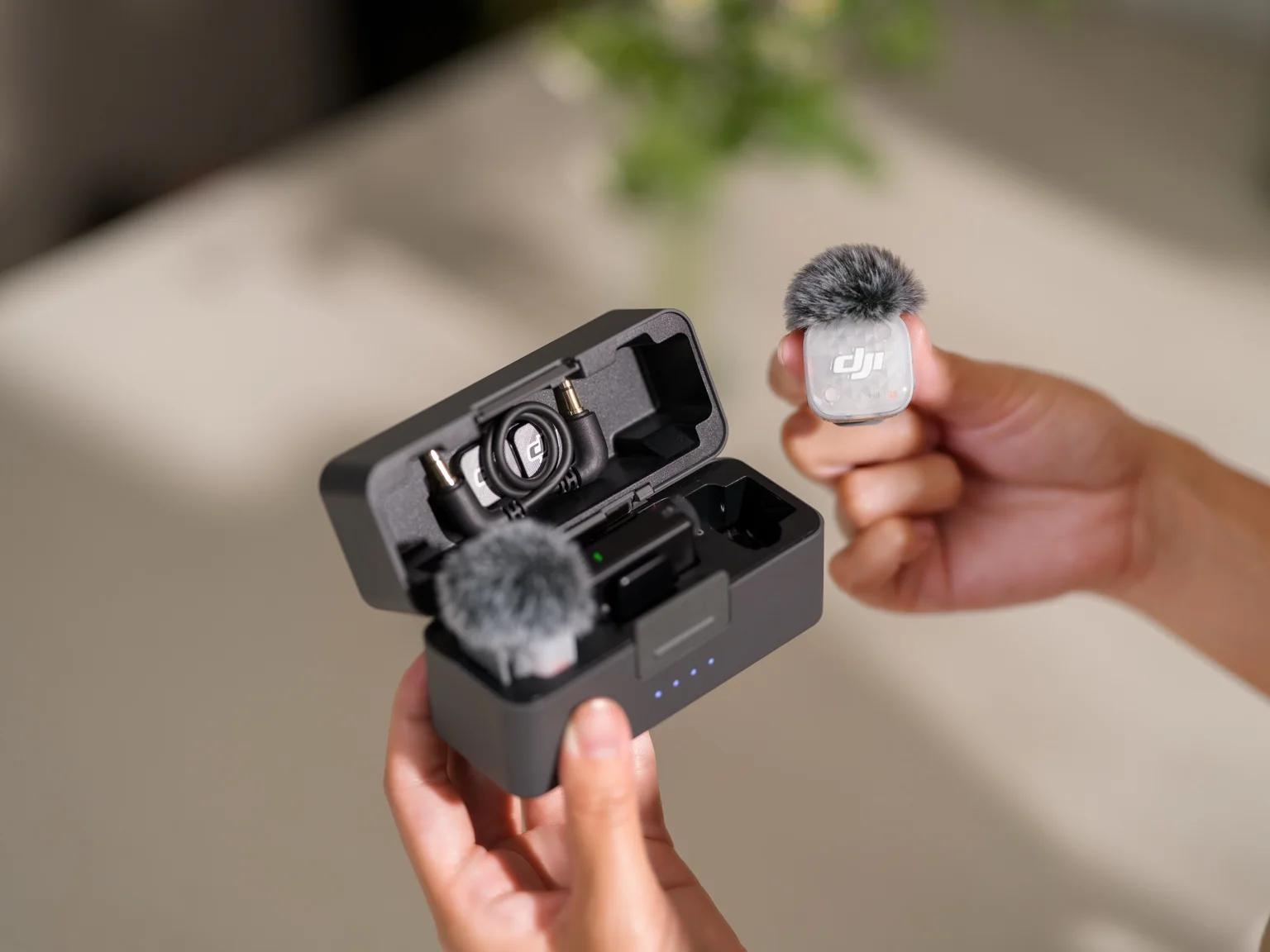En person håller laddningsetuiet till DJI Mic Mini 2S i ena handen och en liten trådlös sändare i den andra.