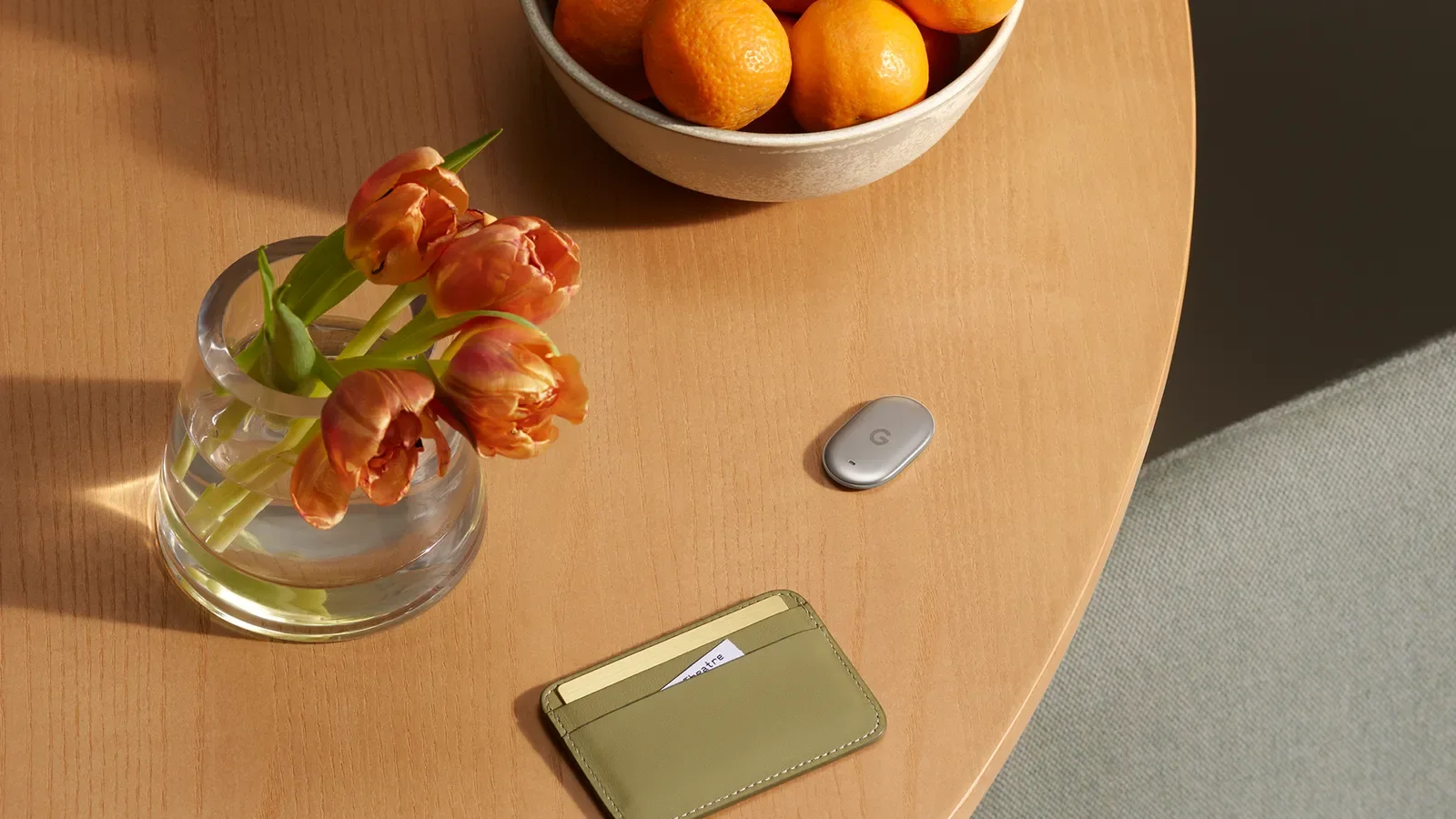Google Pixel Tag ligger på ett träbord bredvid en plånbok och en vas med blommor.
